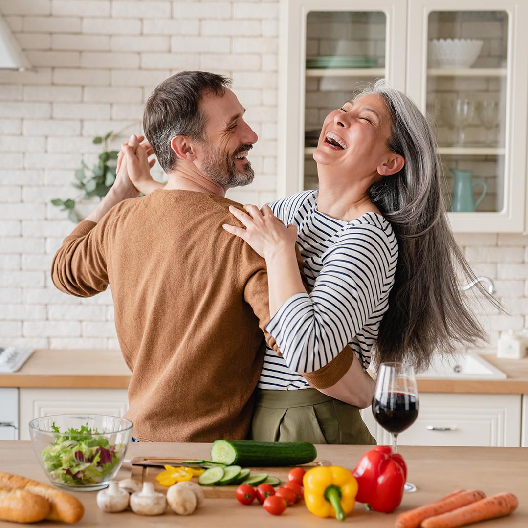 older couple embrace and laughing with fresh fruits and vegetables in foreground